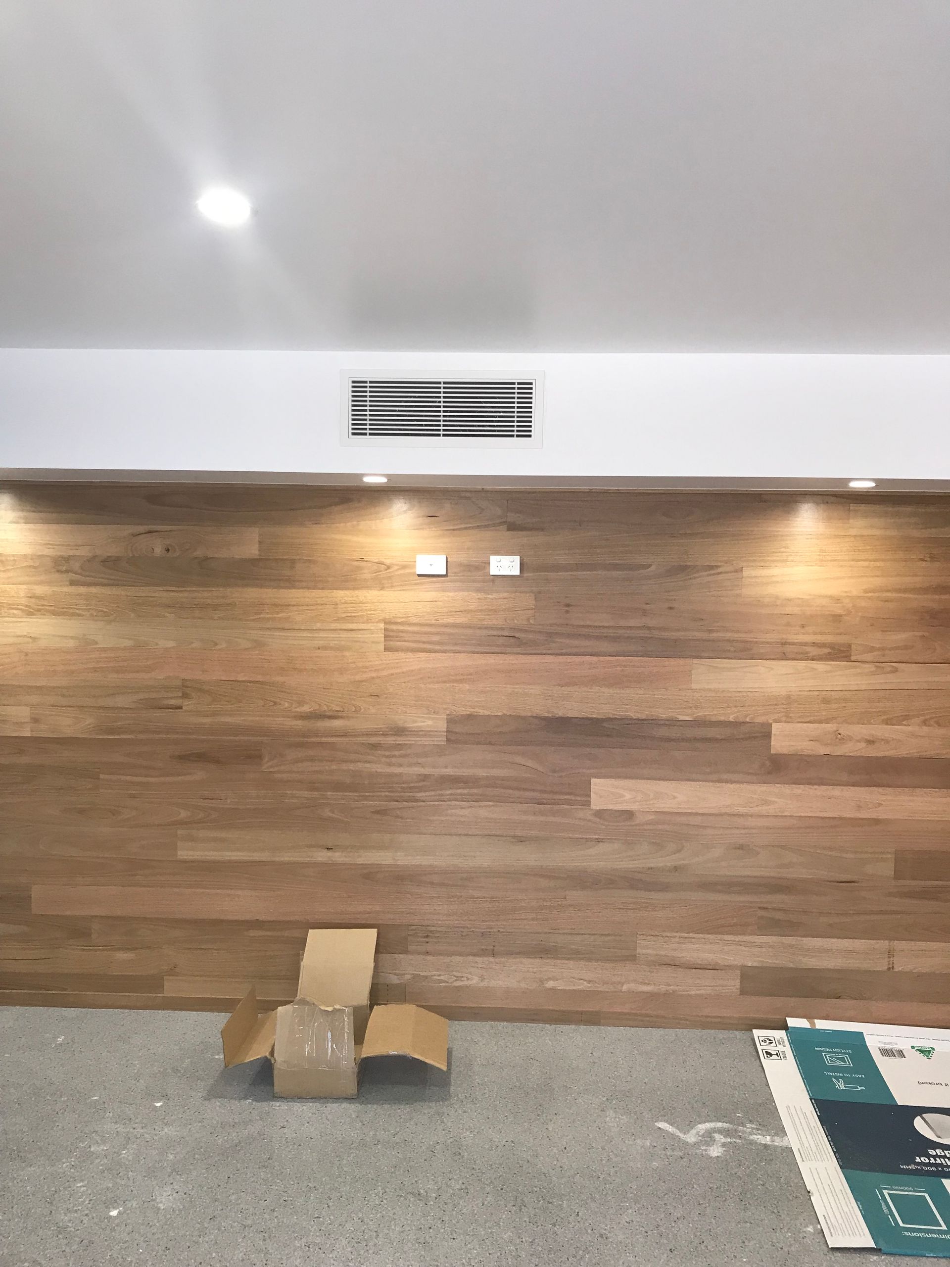 Empty room with wood-paneled wall, white ceiling vent, concrete floor, and a cardboard box on the floor.