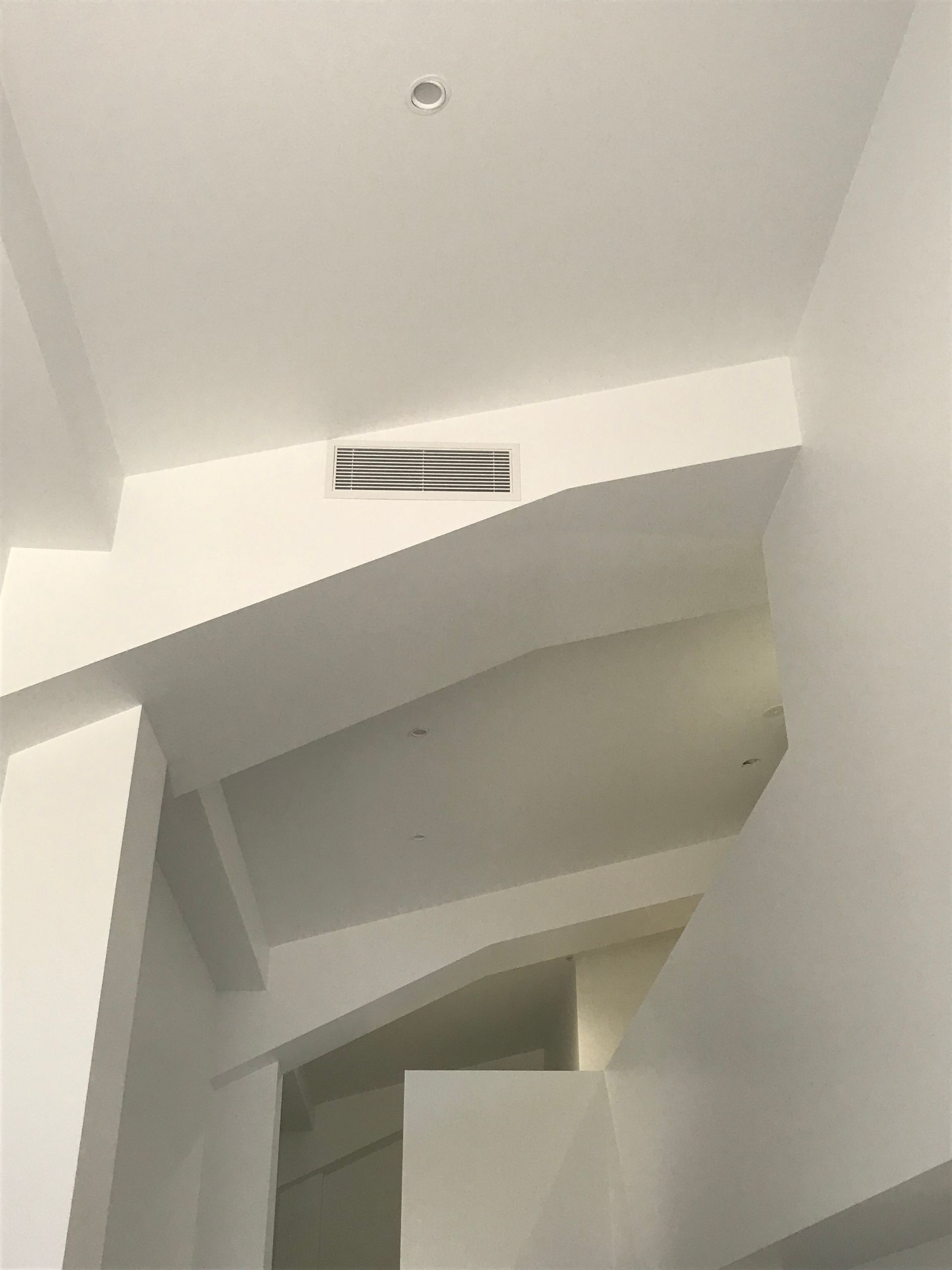 White interior stairwell with angled walls and a small rectangular vent near the ceiling