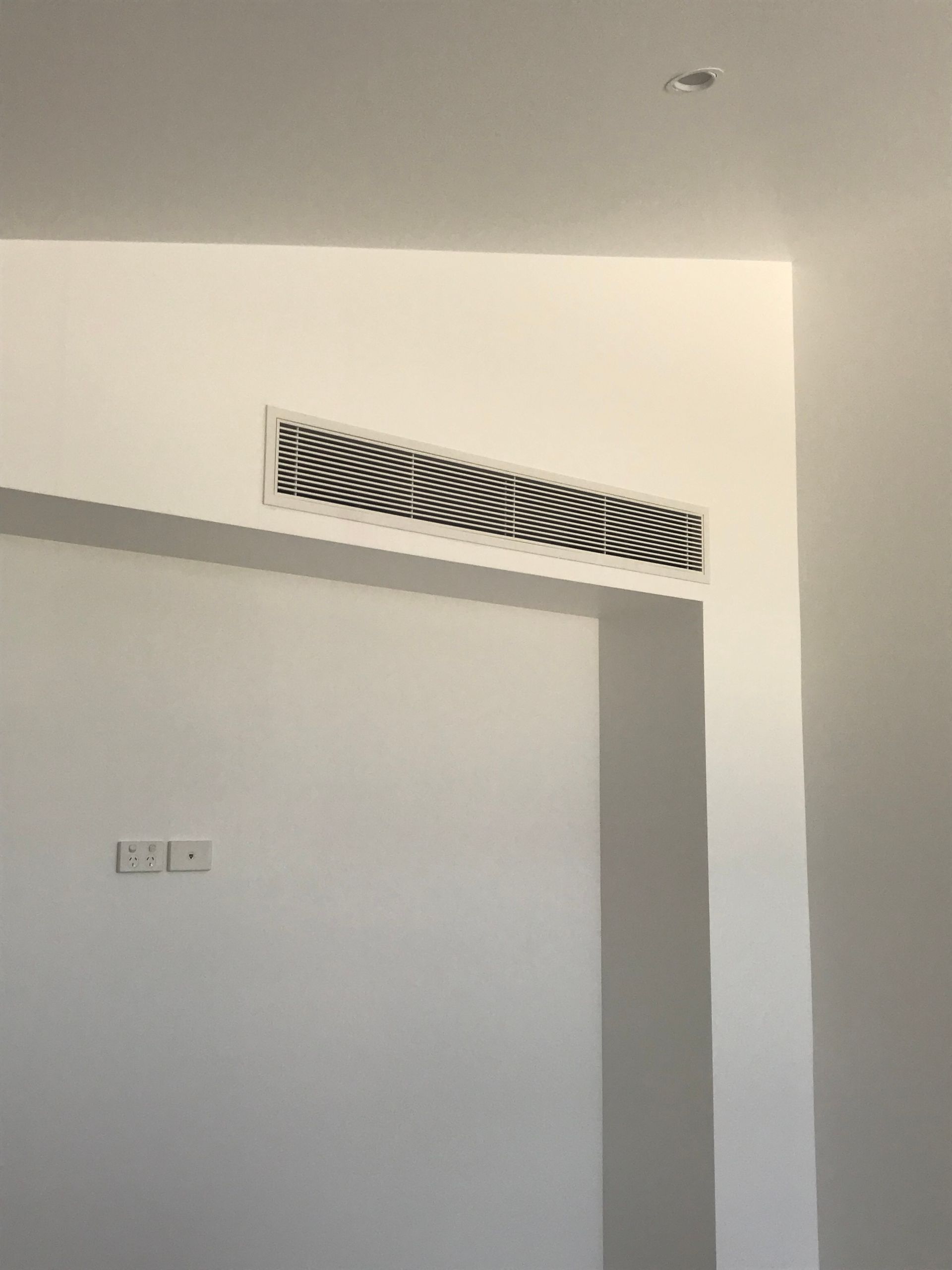 Interior wall with a diagonal white air vent above a doorway on a light gray wall