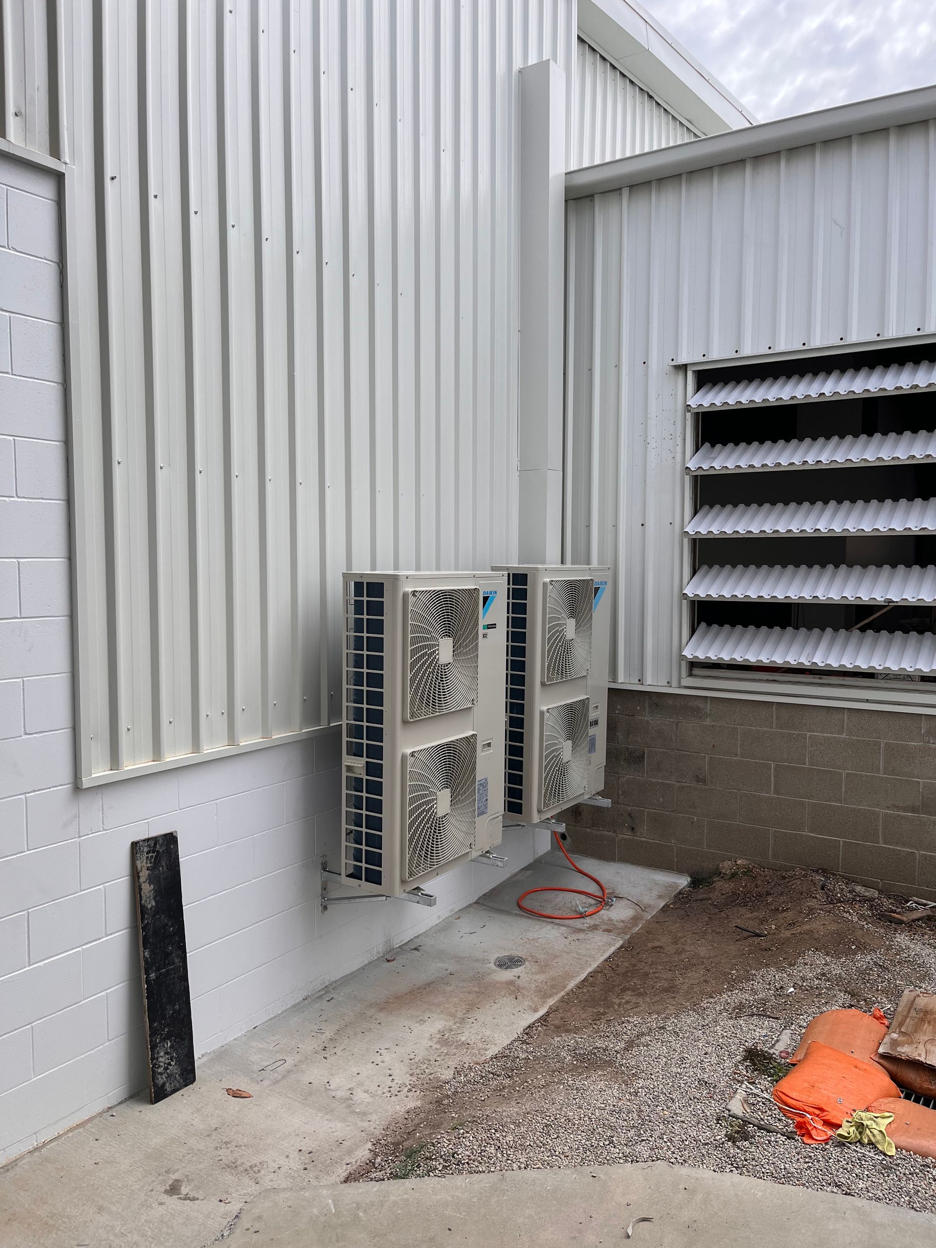 Outdoor utility equipment mounted on a white building wall beside vents and gravel ground