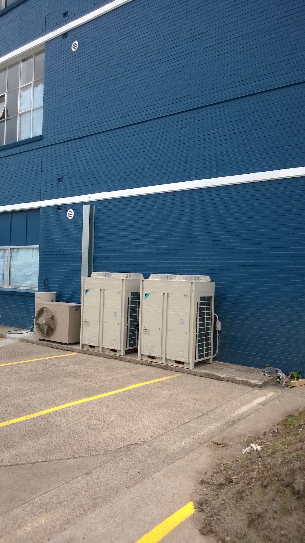 Blue industrial building exterior with beige HVAC units along a concrete parking area