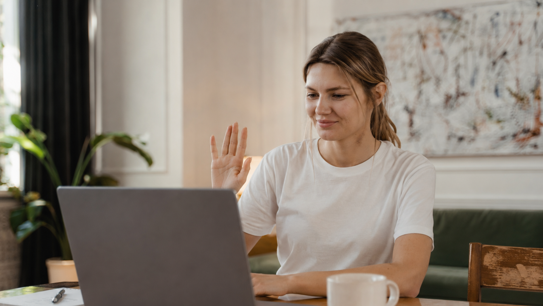 Woman waving during a video call at a laptop in a home office
