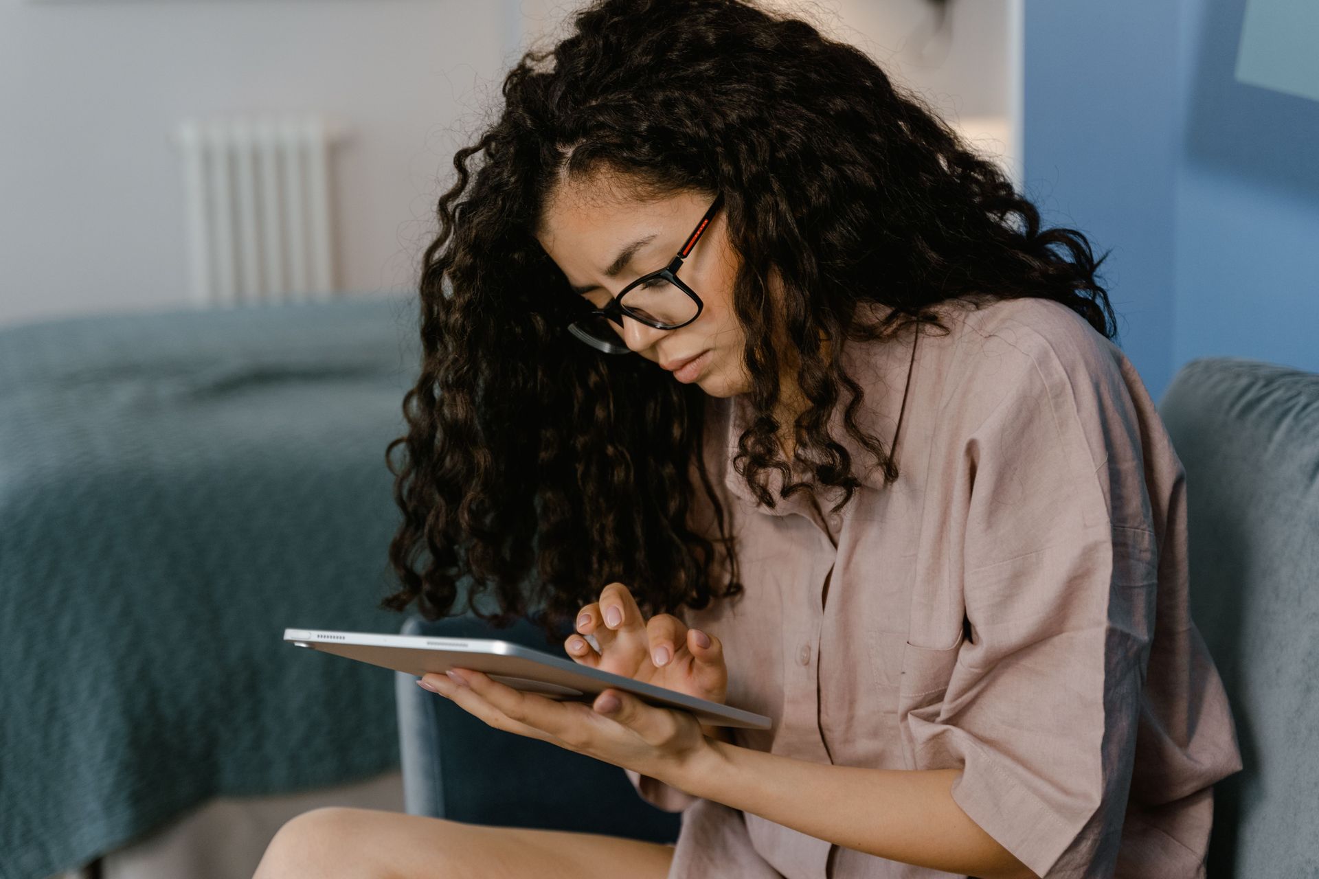 Person with curly hair using a tablet on a sofa in a living room