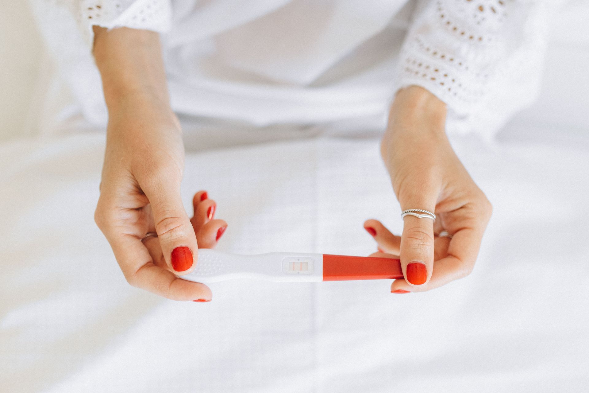 Hands holding a red-and-clear pregnancy test on a white background
