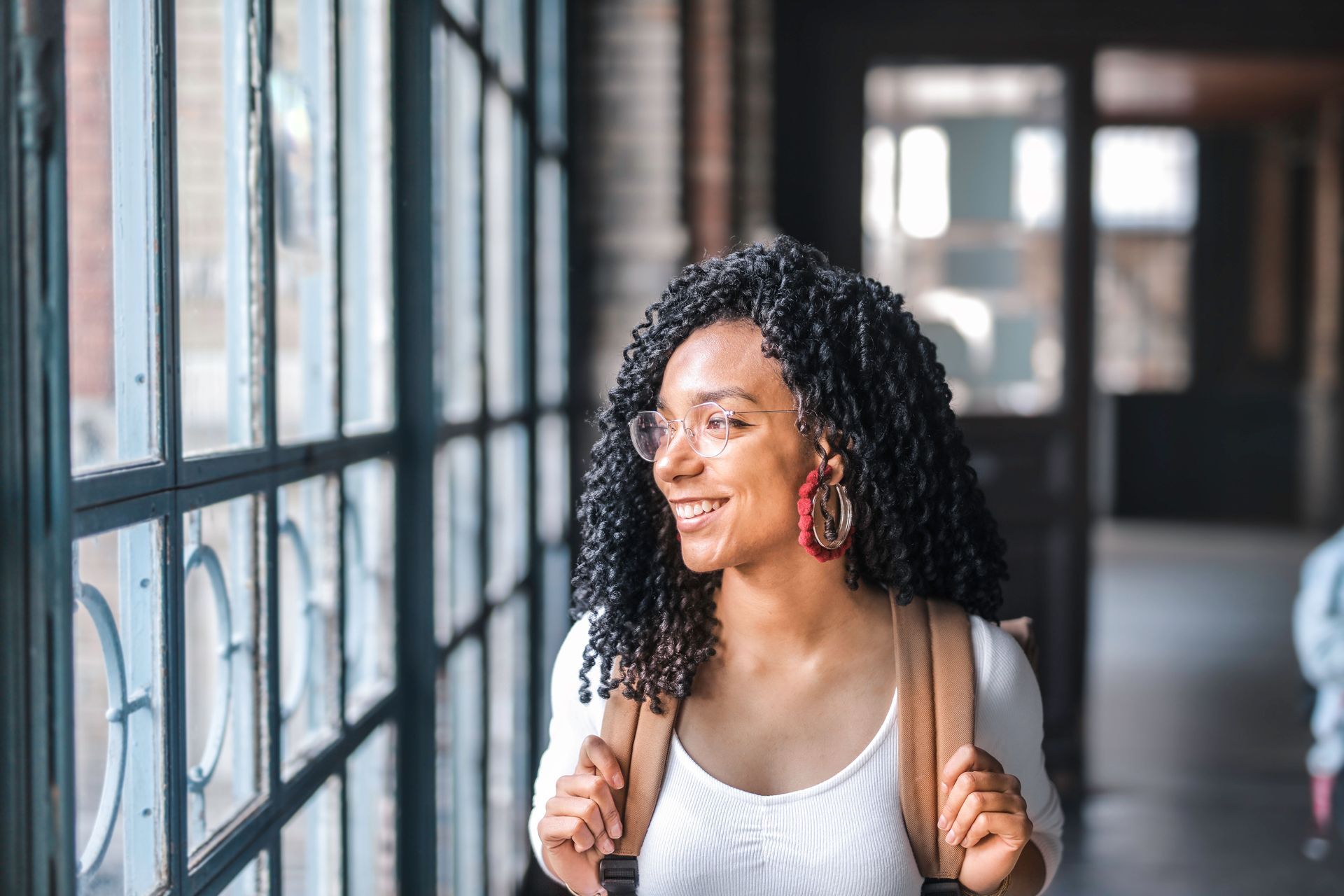 Woman with backpack smiling by large windows in a bright hallway