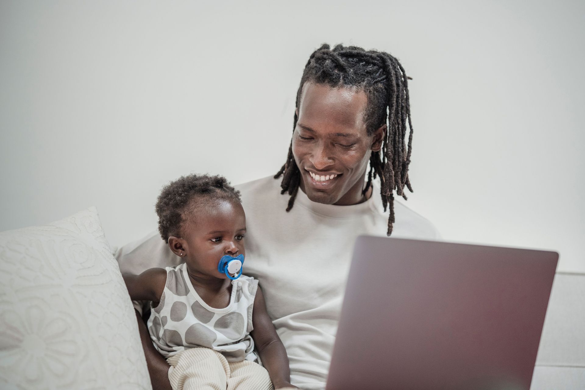 Parent smiling with child on a laptop in a bright living room