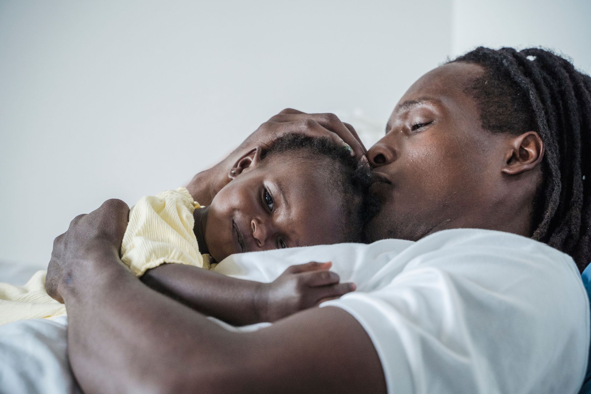 A father and son embracing on a couch, one kissing the other’s forehead.