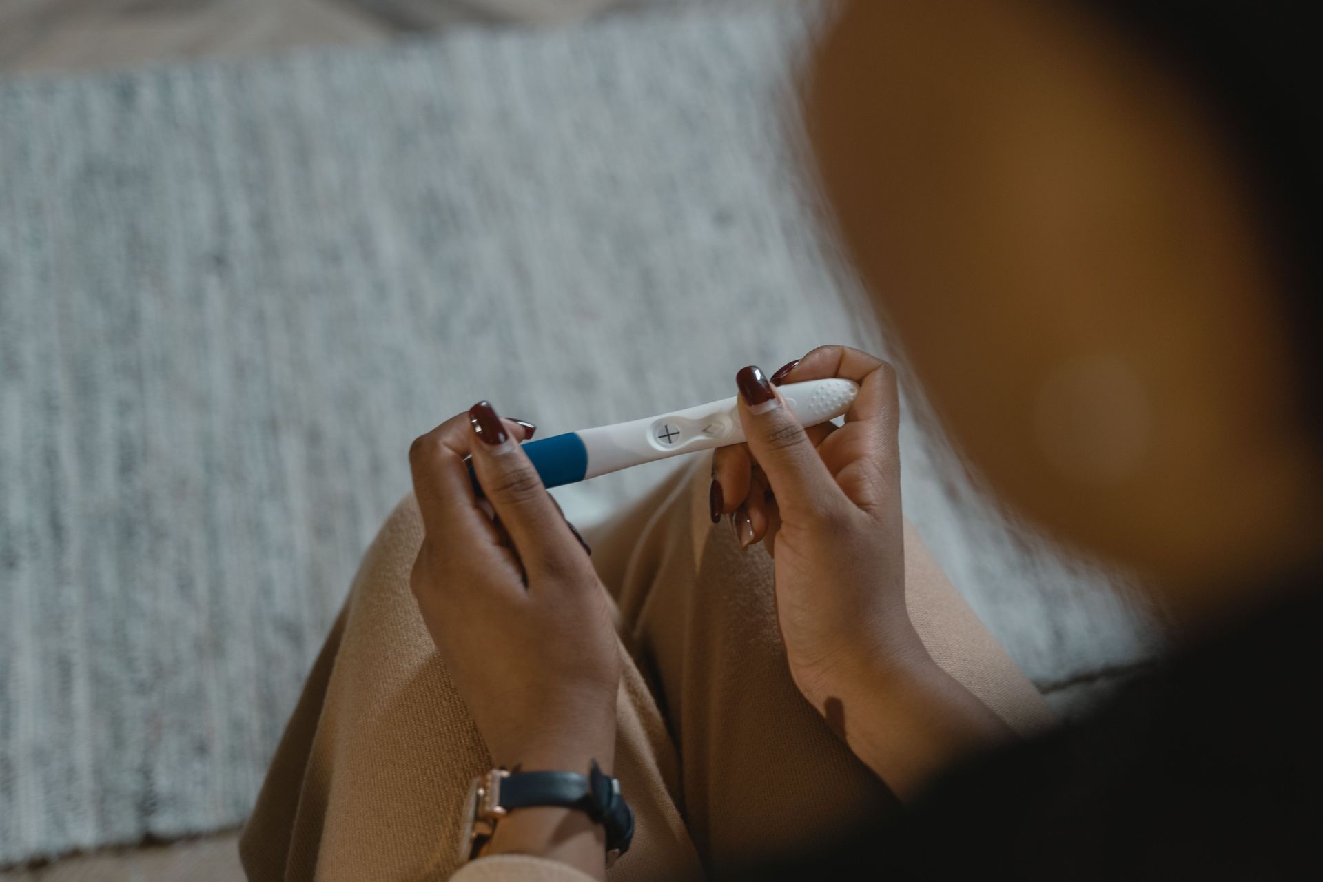 Hands holding a white-and-blue pregnancy test, with a blurred person in the foreground.
