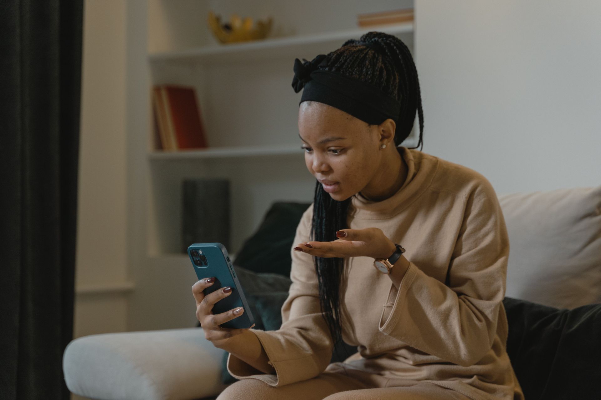Woman in beige sweater on couch video chatting on smartphone, smiling and gesturing in a living room