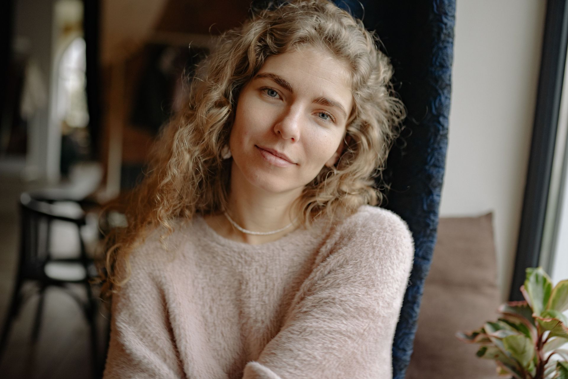 Smiling person in a pink sweater leaning by a window in a cozy café