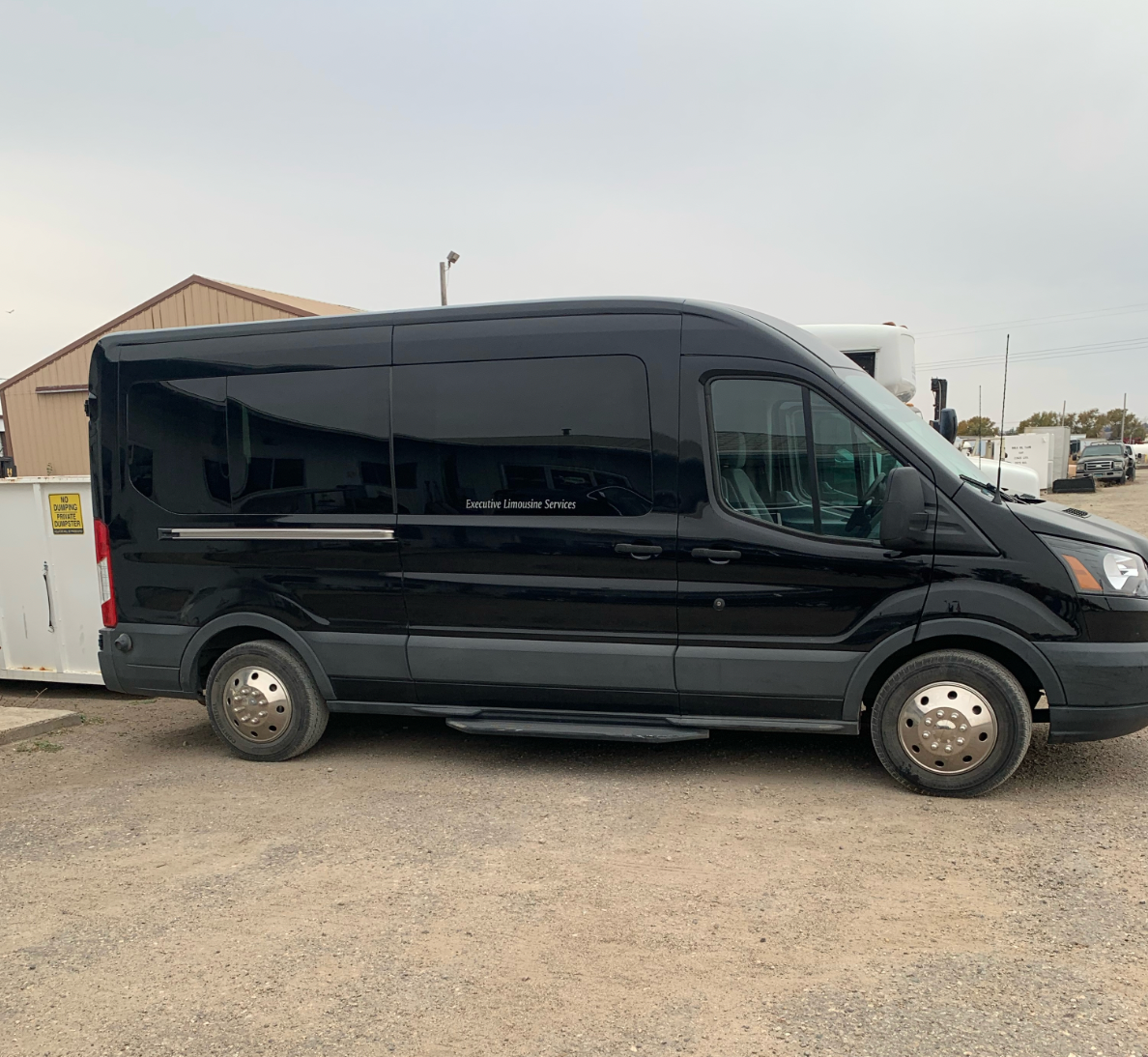 A black van is parked in a gravel lot.