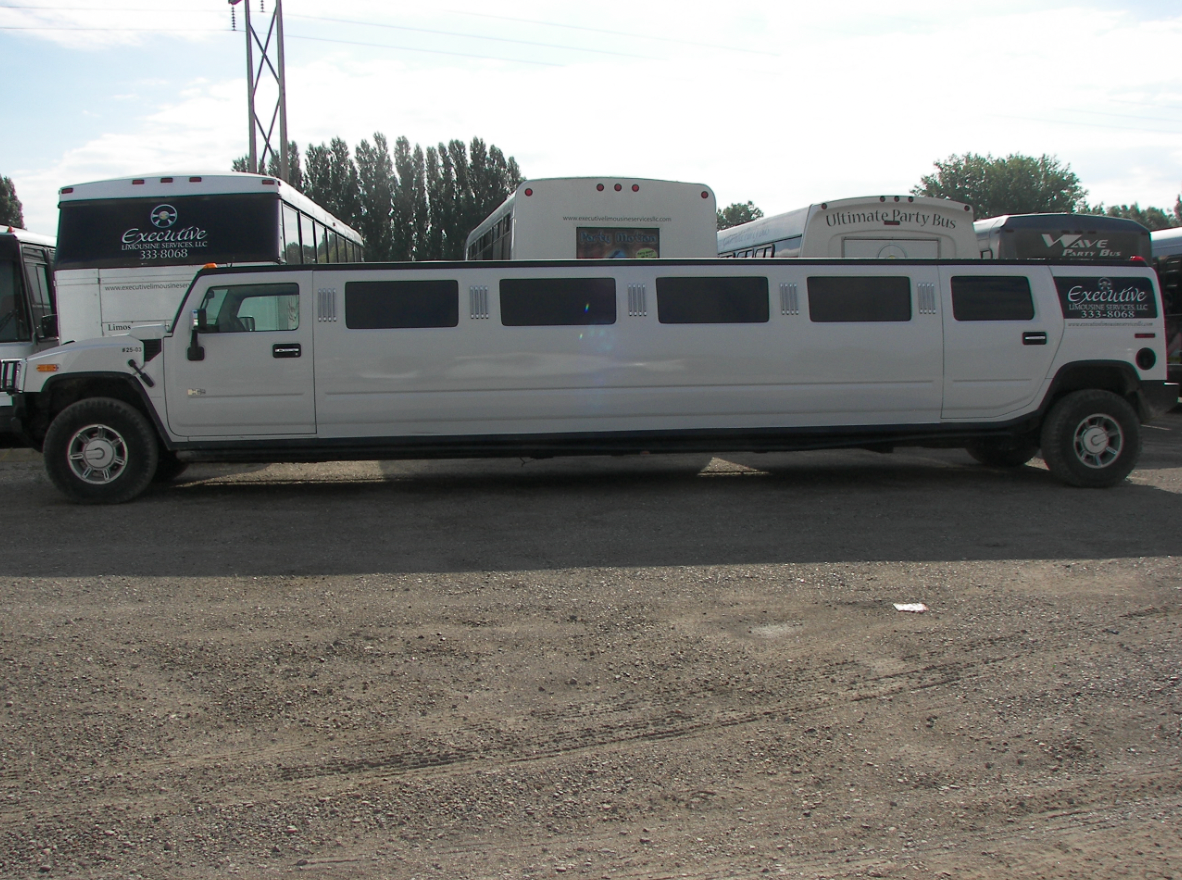 A white hummer limousine is parked in a gravel lot.