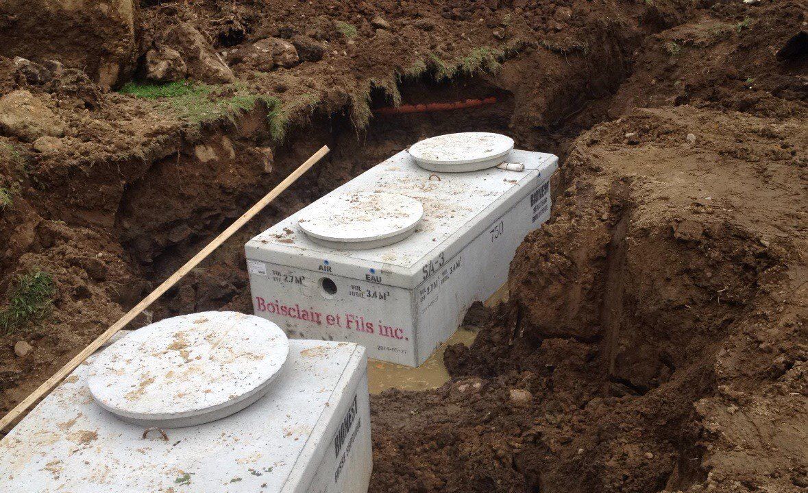 Deux fosses septiques rectangulaires en béton dans une tranchée excavée, couvercles visibles.