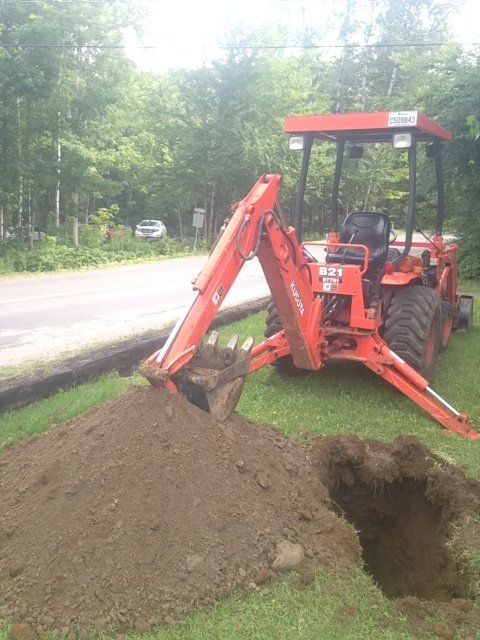 Un tracteur orange creuse un trou dans l'herbe.