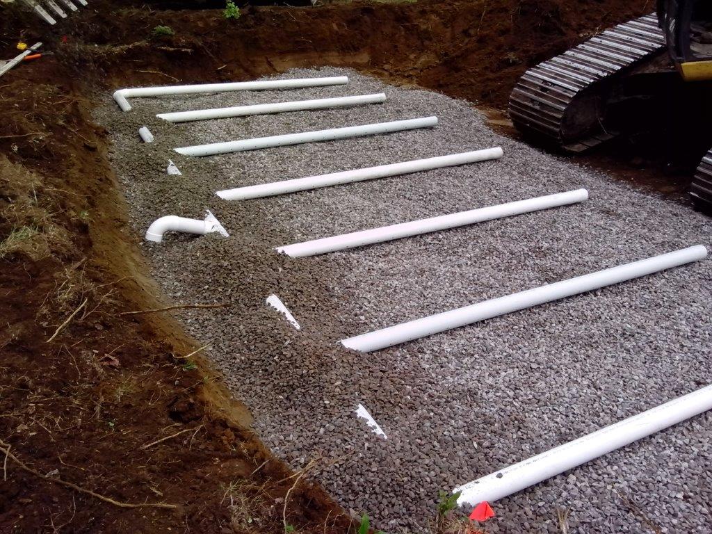 Une rangée de tuyaux blancs posés sur du gravier à côté d'un bulldozer.
