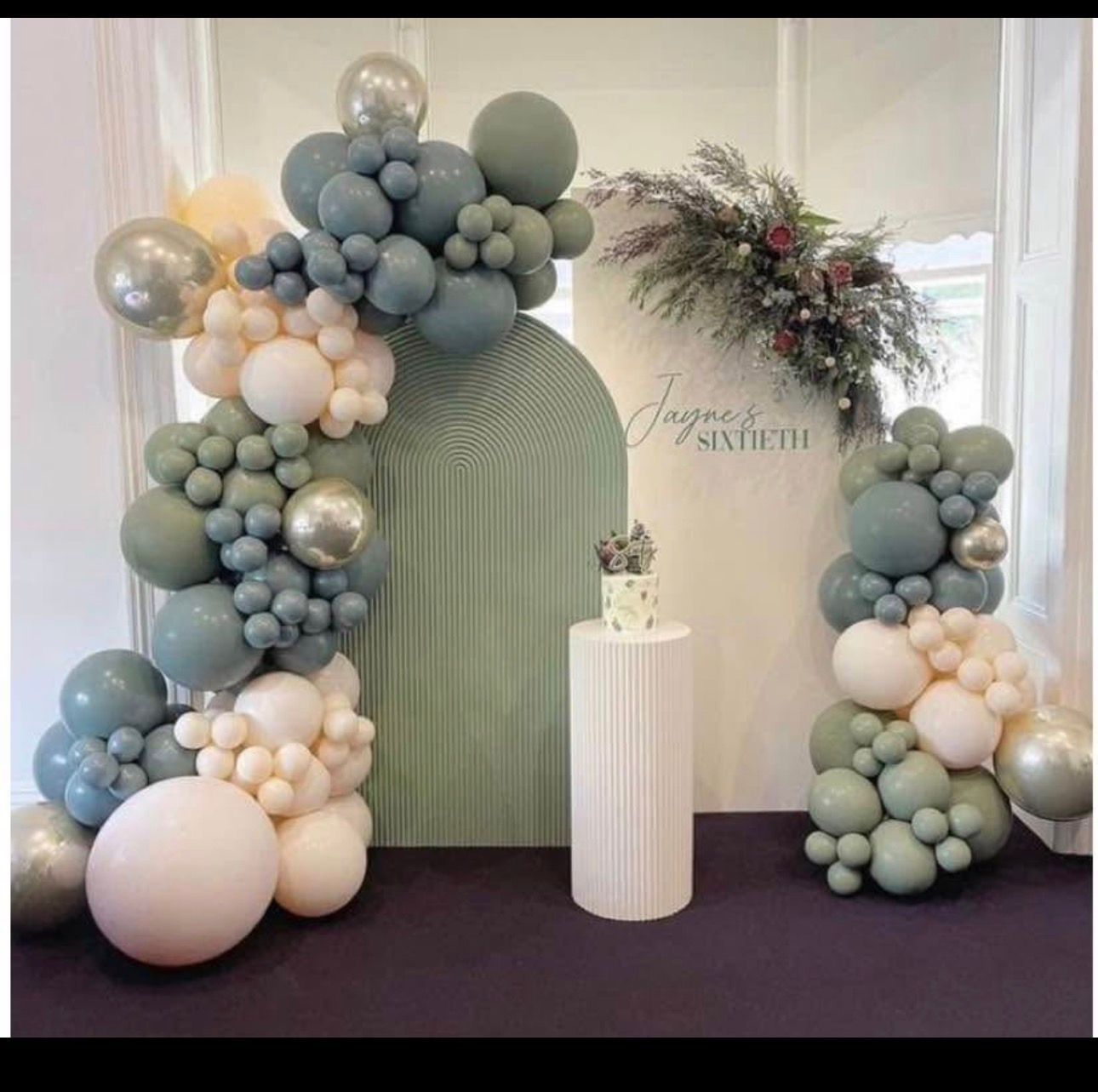 Pastel balloon arch and floral backdrop with a small white pedestal at an elegant celebration setup
