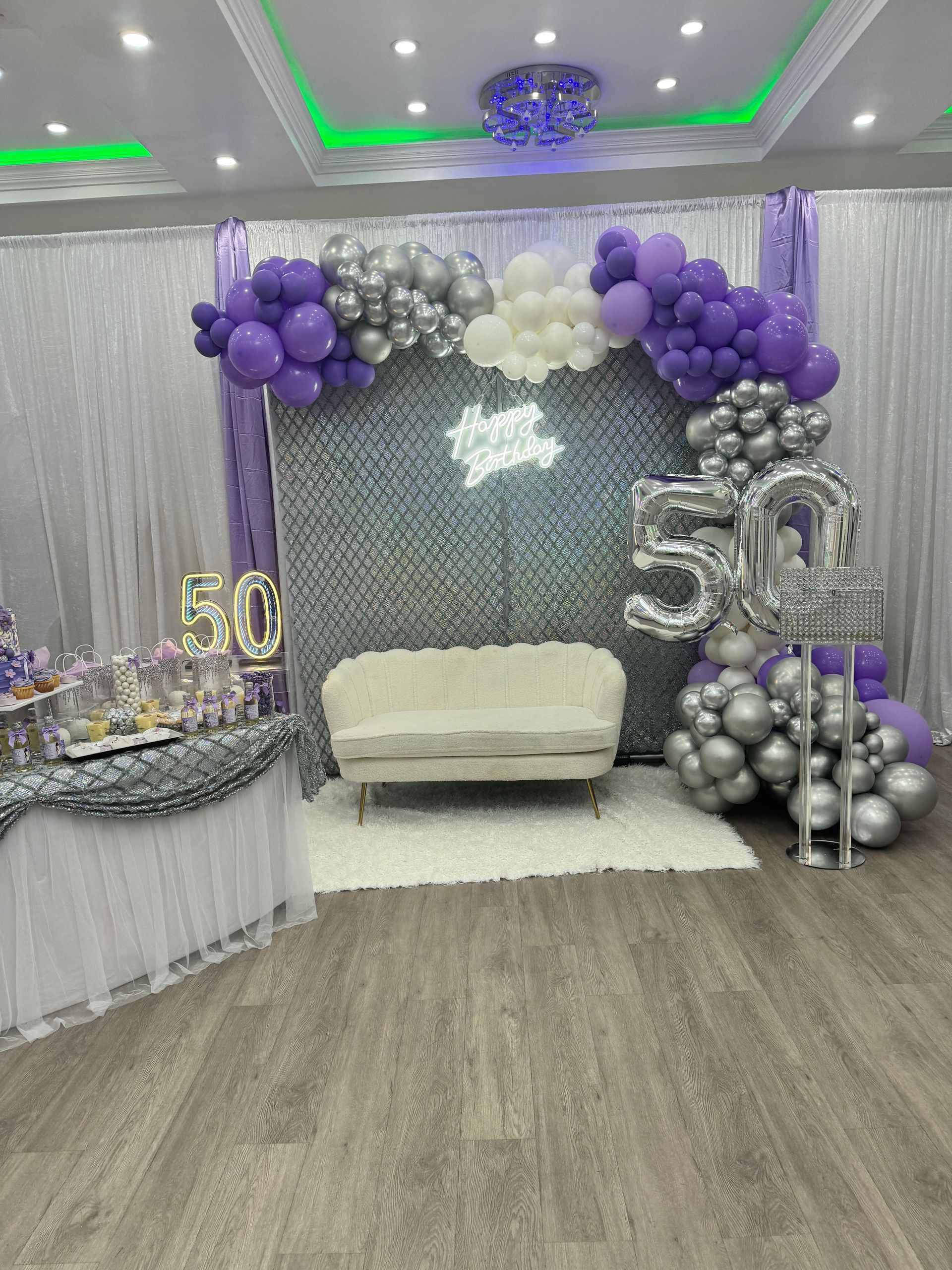 Purple-and-silver 50th birthday party backdrop with balloons, couch, and sparkling decor