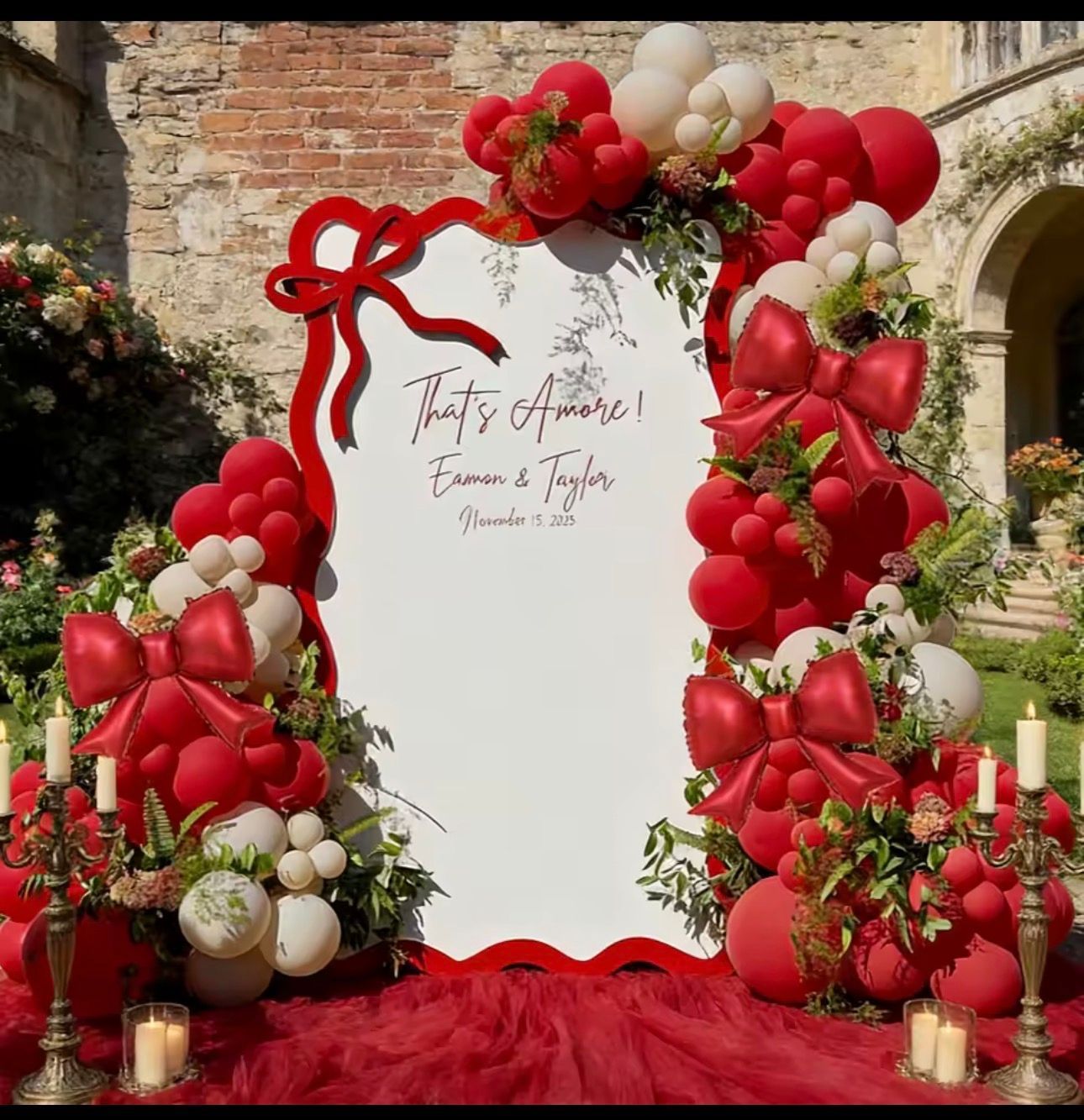 Red and white balloon arch framing a wedding welcome sign on a stone courtyard backdrop