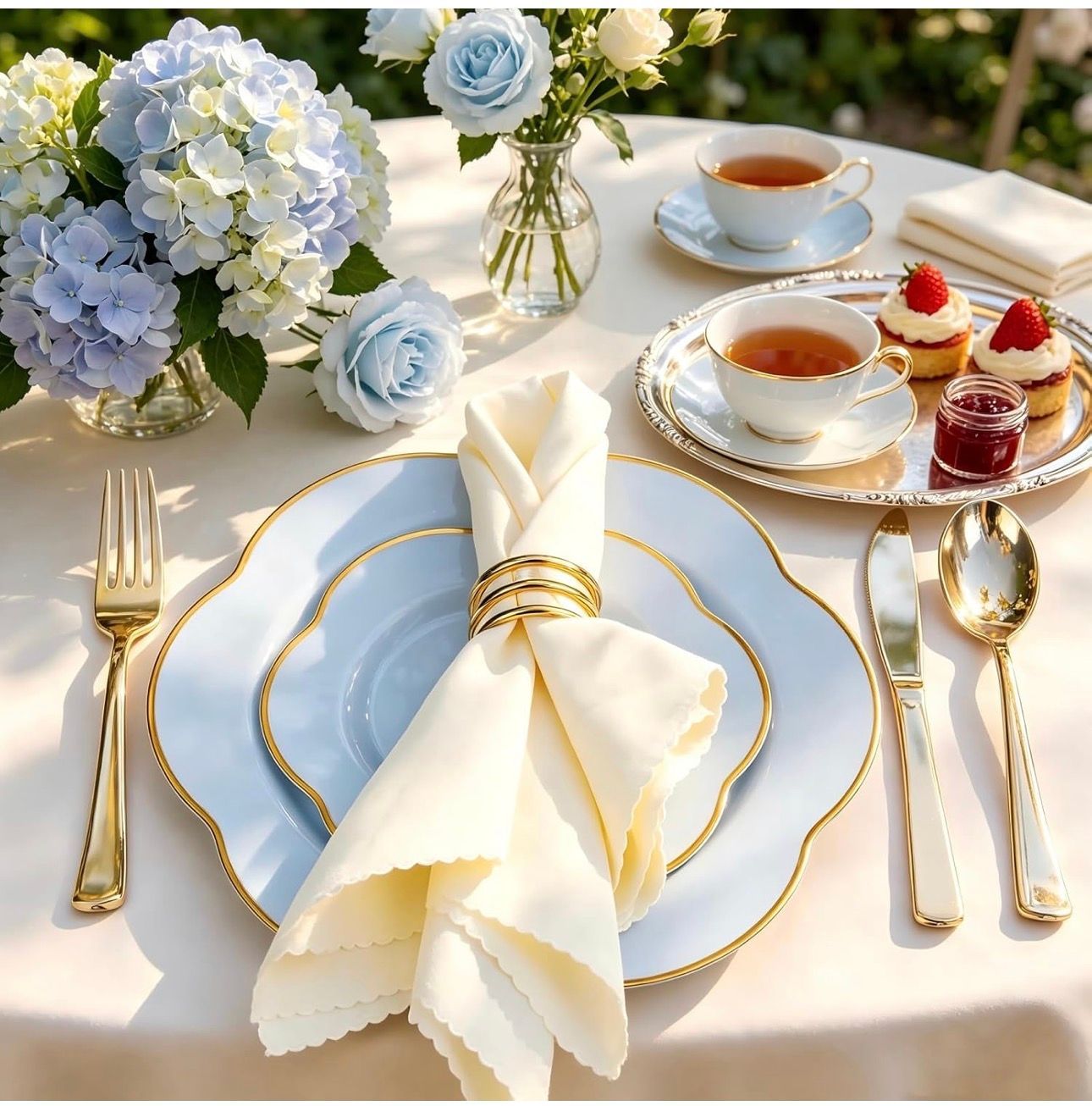 Elegant tea table with blue-and-gold china, pastries, flowers, and folded napkin settings in soft sunlight
