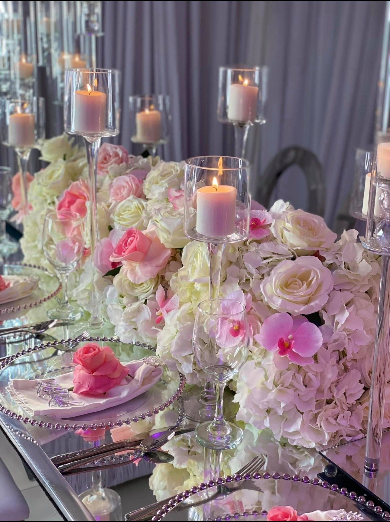 Elegant banquet table with pink and white flowers, candles, and mirrored place settings under soft draped decor