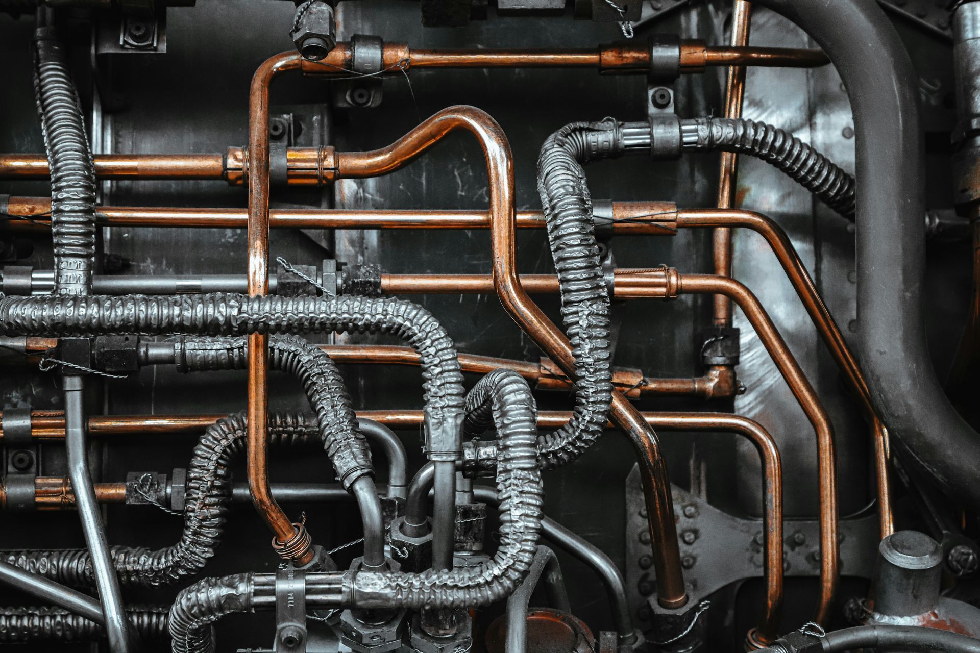 Close-up of intertwined copper and gray industrial pipes against a dark background