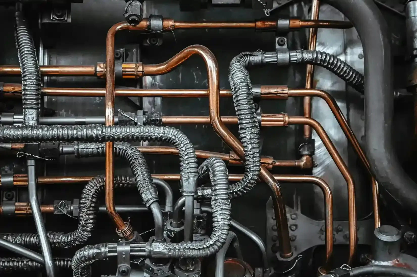 Dense network of copper and gray pipes and conduits in an industrial wall system