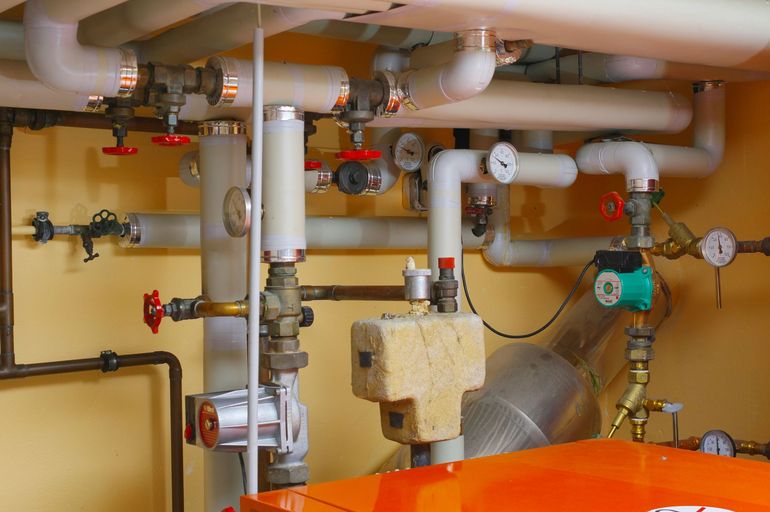 Industrial piping and valves in a utility room, with white and green pipes against a yellow wall.