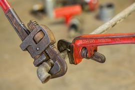 Rusty pipe wrench gripping a metal pipe beside a red adjustable wrench on a blurred workbench