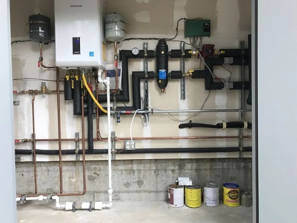 Basement wall with water heater, pipes, valves, and maintenance cans on the floor
