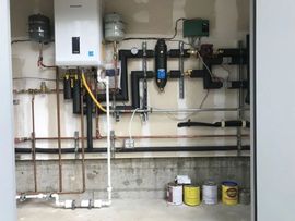 Basement wall with water heater, pipes, valves, and maintenance cans on the floor