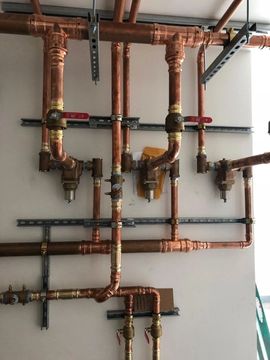 Copper and black pipe manifold installation on a white wall, with multiple valves and horizontal runs