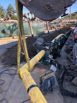Yellow pipe section under construction at an outdoor site, with equipment and rubble nearby.