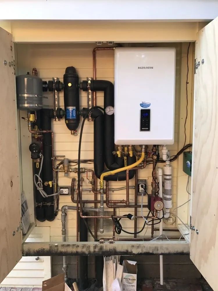 Open utility cabinet with boiler, pipes, tanks, and plumbing equipment inside