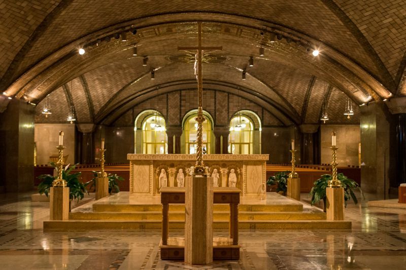 Church altar beneath arched ceiling with stained glass and candles, warmly lit interior