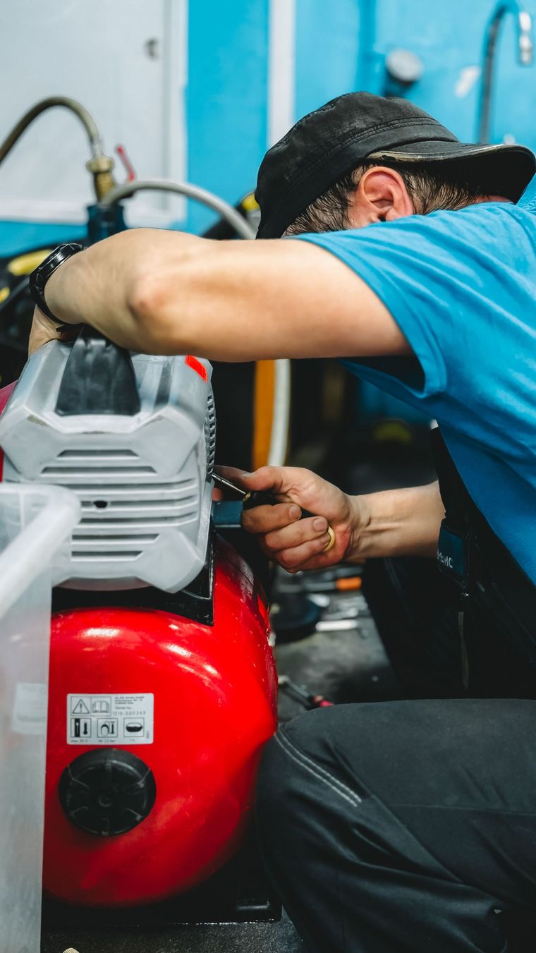Technician repairing a red air compressor with a wrench in a workshop