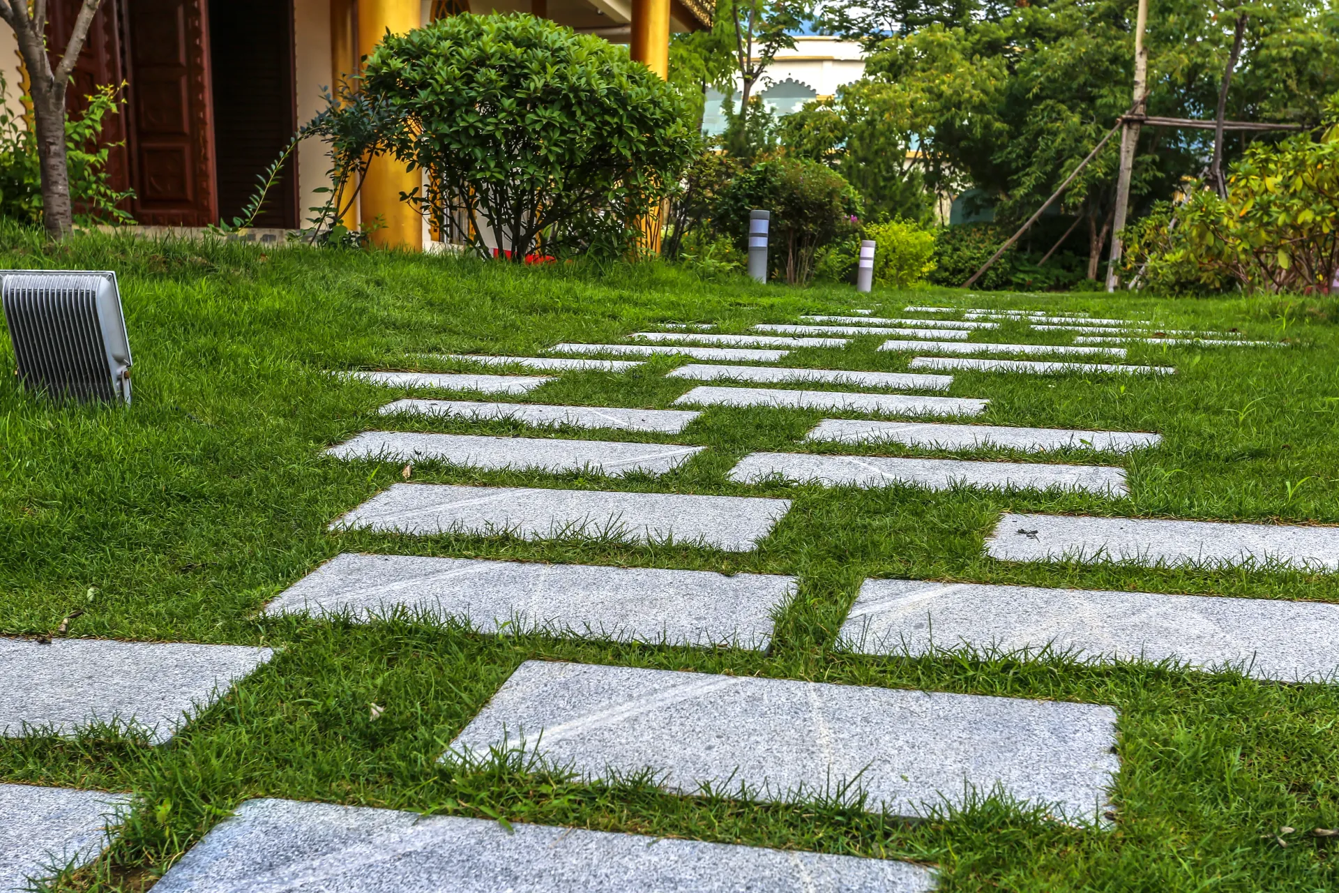 White stepping stones through a green garden lawn with trees and shrubs in the background