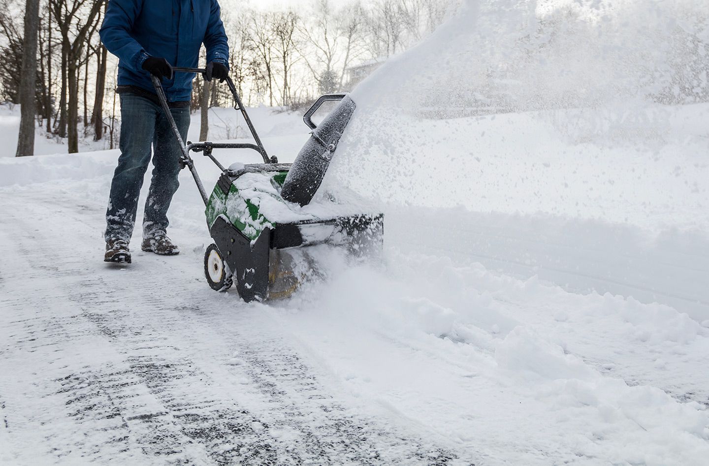Person using a snowblower, clearing a snowy path. Winter scene, snow blowing in air.
