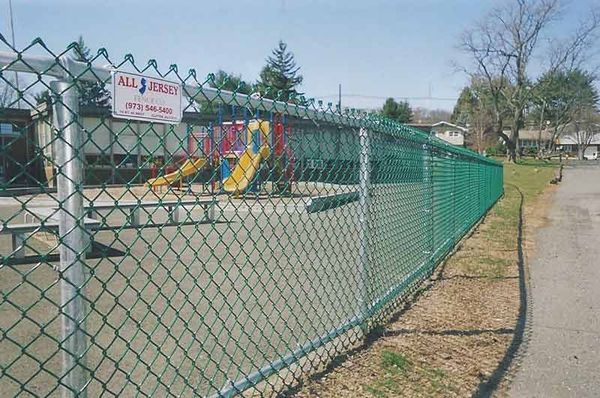 A chain link fence surrounds a playground with a sign that says all jersey