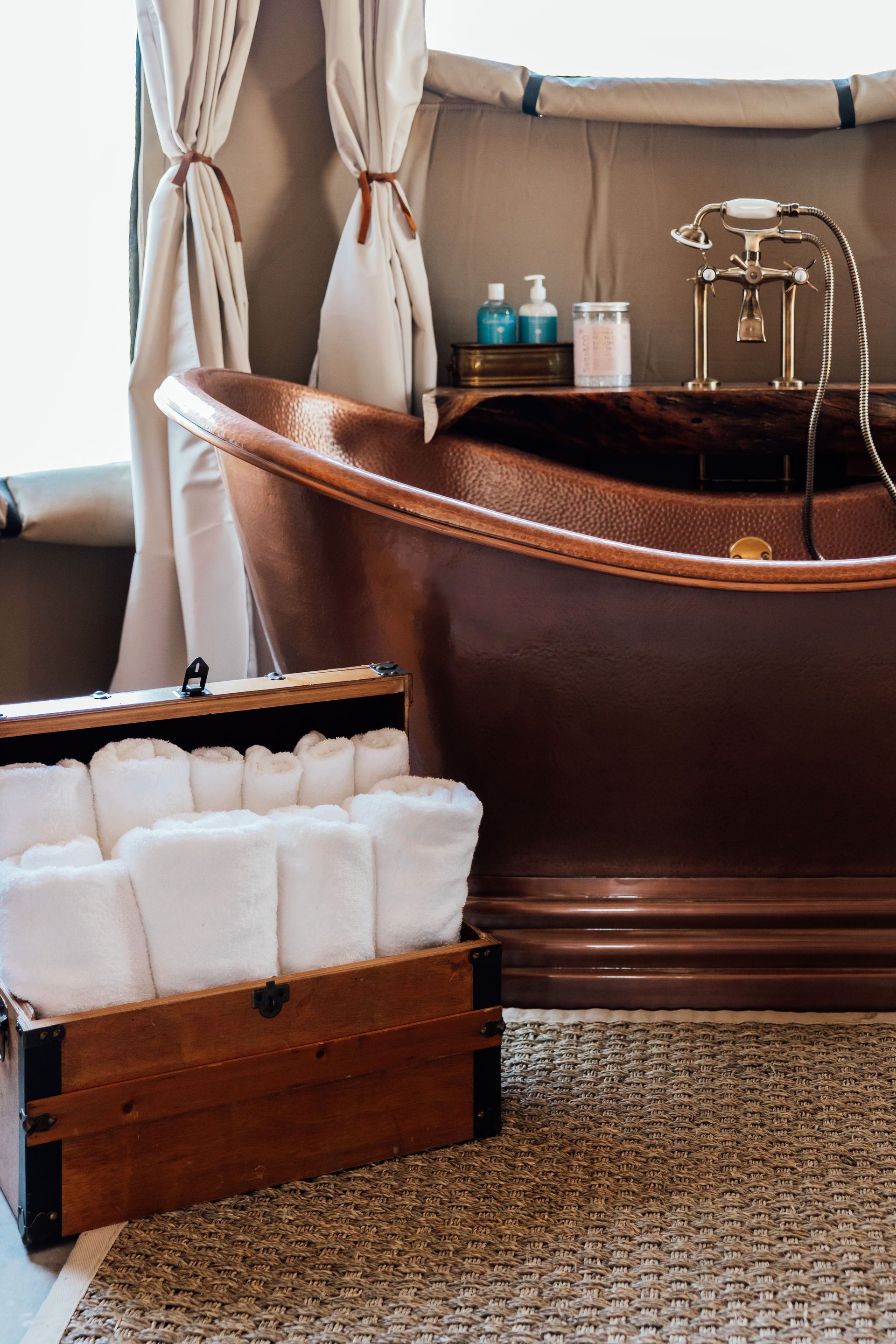 Copper bathtub in luxury bathroom with rolled white towels and accessories.
