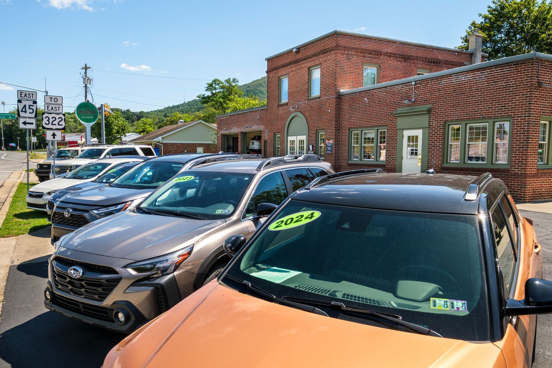 Cars parked in front of a brick building with a sign, under a sunny sky. | Boalsburg Car Co.