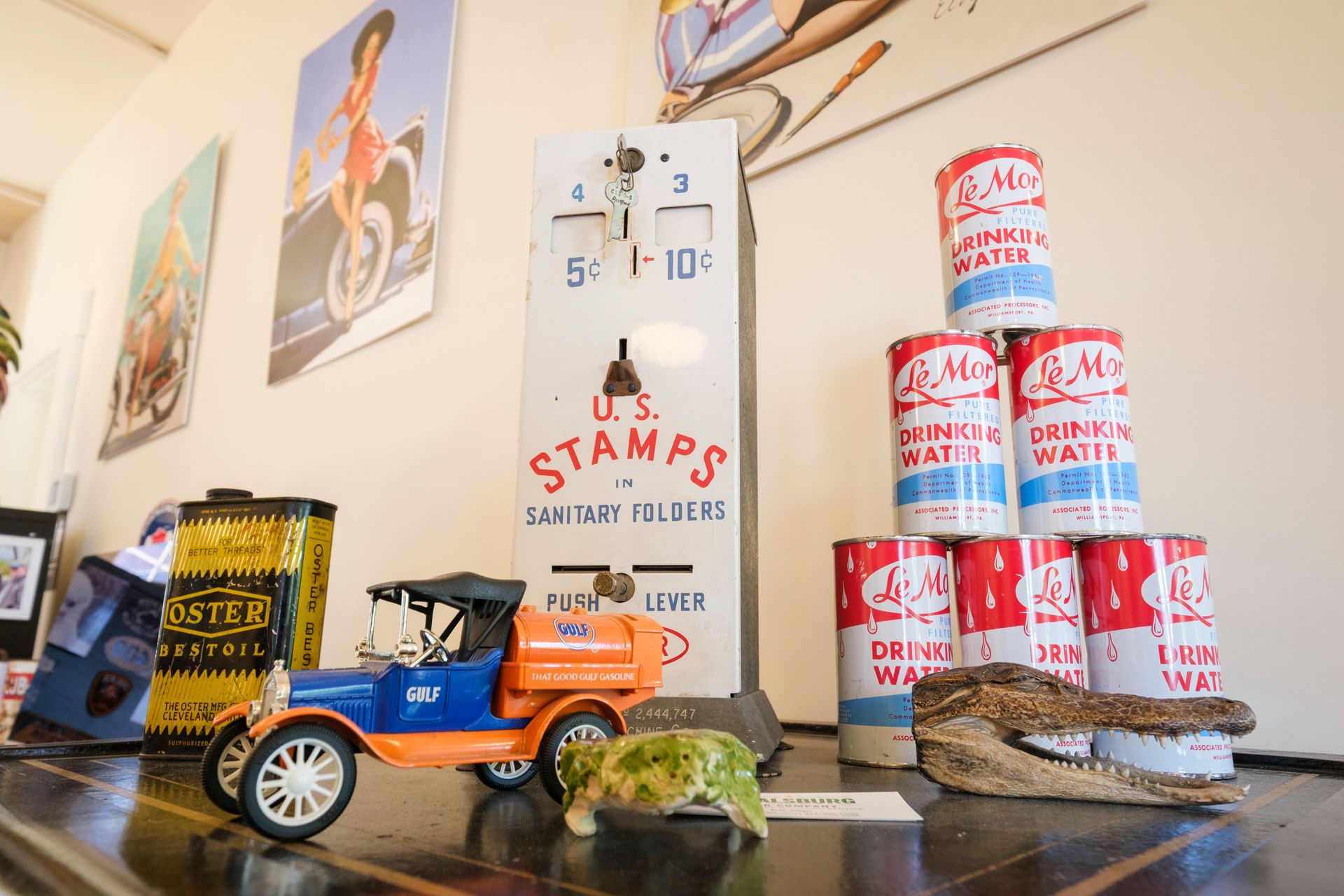 Shelf with vintage items: toy car, stamp machine, water cans, poster, and alligator head. | Boalsburg Car Co.