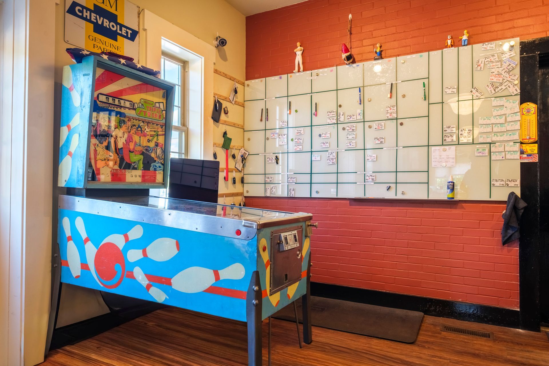 Pinball machine in a room with a whiteboard, brick wall, and various decorations. | Boalsburg Car Co.