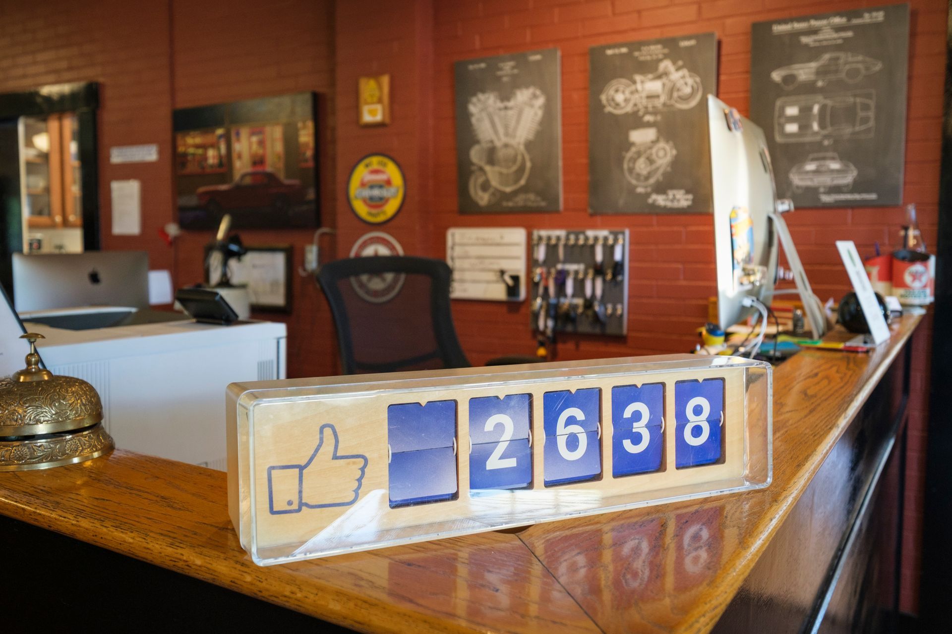 A counter on a front desk shows 2638 likes, with a thumbs-up icon. Red brick wall and posters in the background. | Boalsburg Car Co.