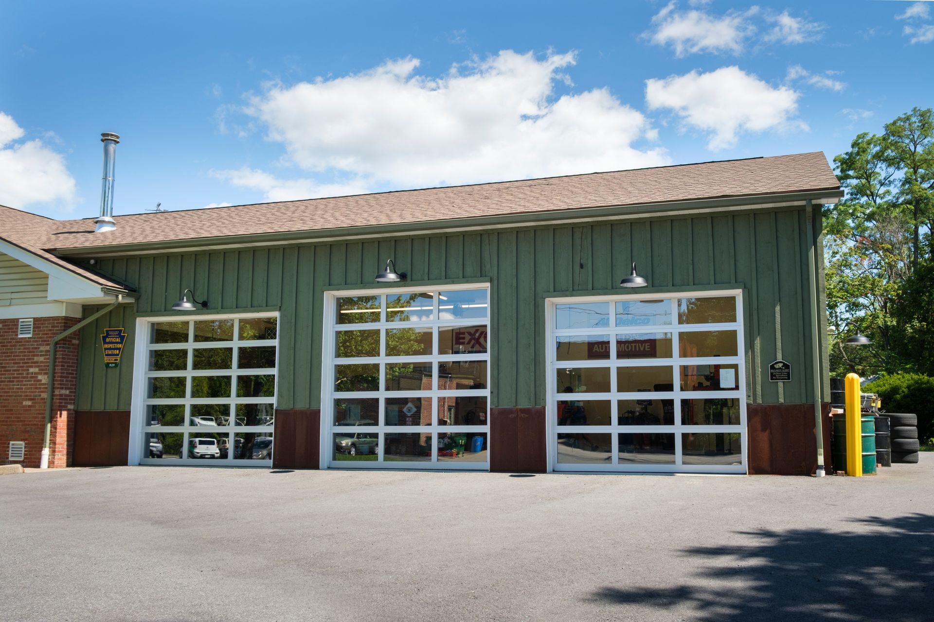 Green building with three glass garage doors, brown roof, and asphalt driveway. | Boalsburg Car Co.