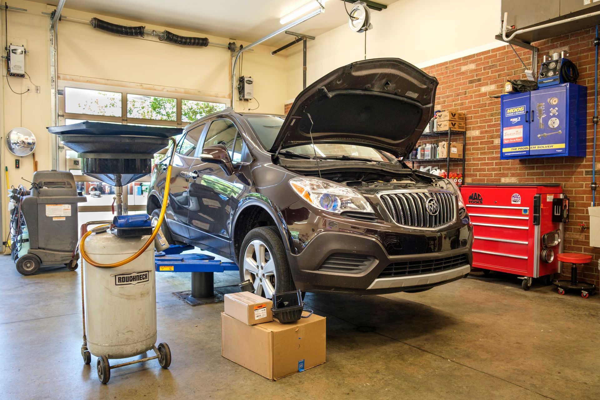 A dark SUV on a lift in a garage with the hood open, ready for repair. | Boalsburg Car Co.
