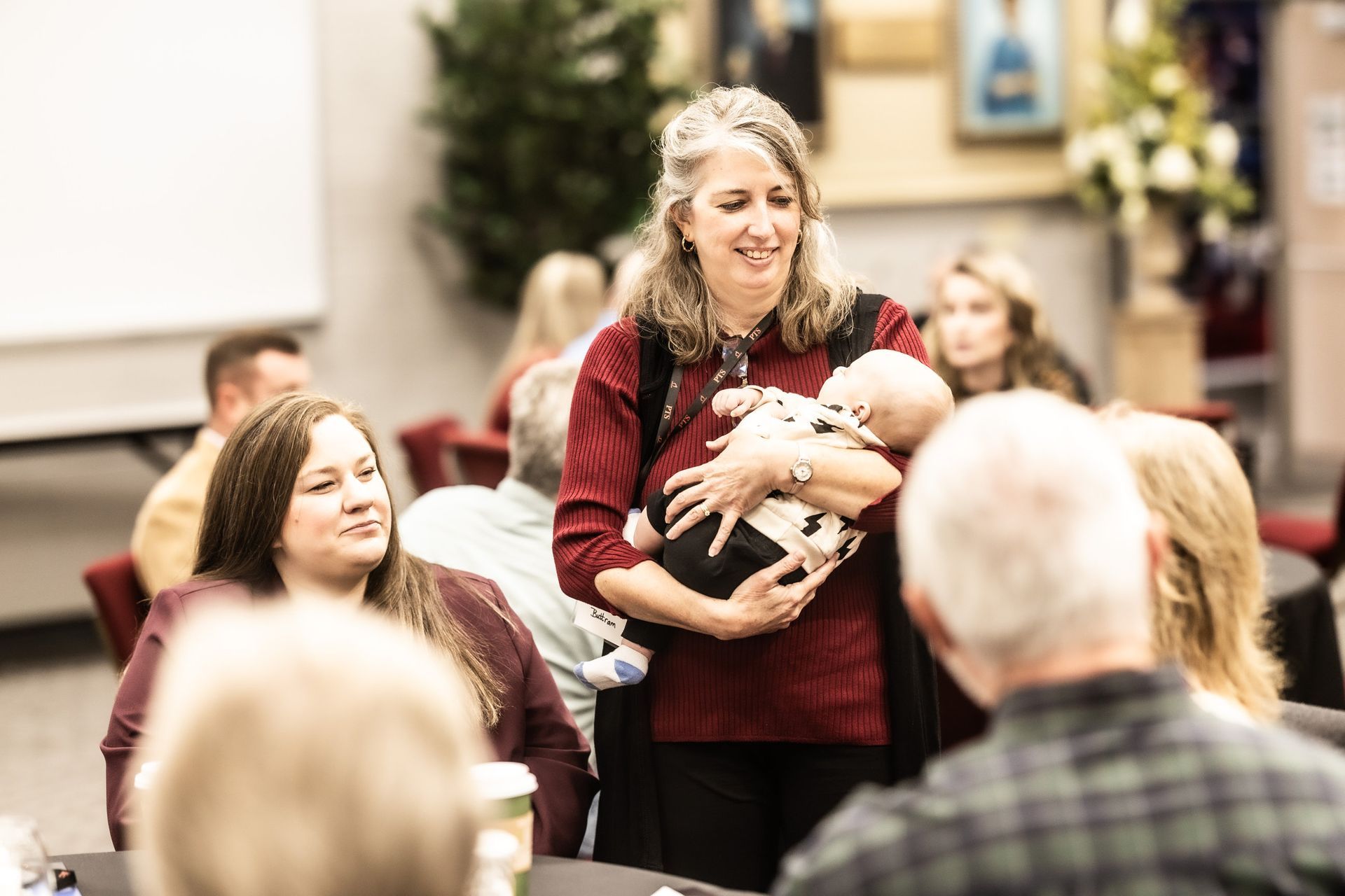 A woman is holding a baby in her arms in front of a group of people.