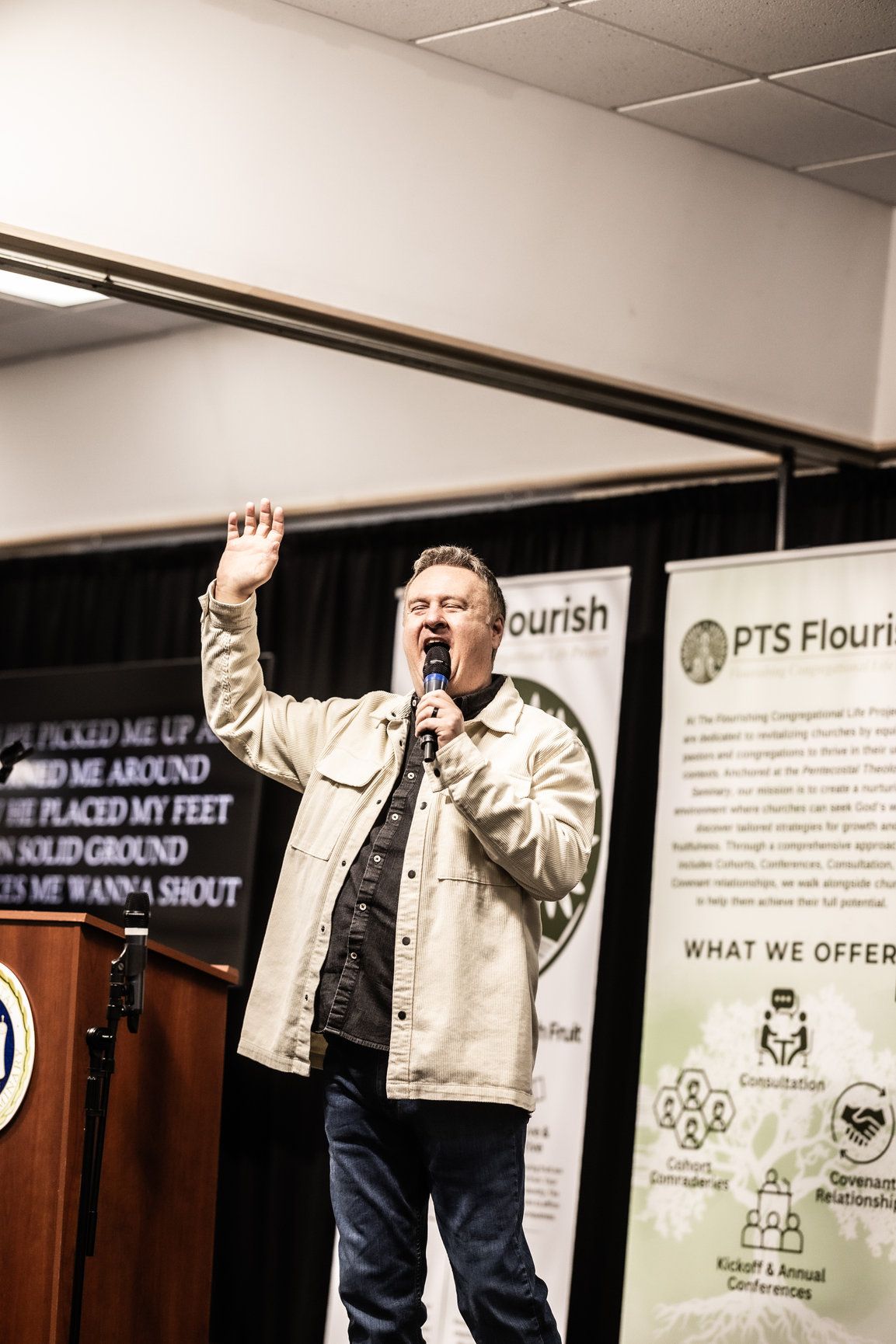 A man singing into a microphone in front of a sign that says nourish