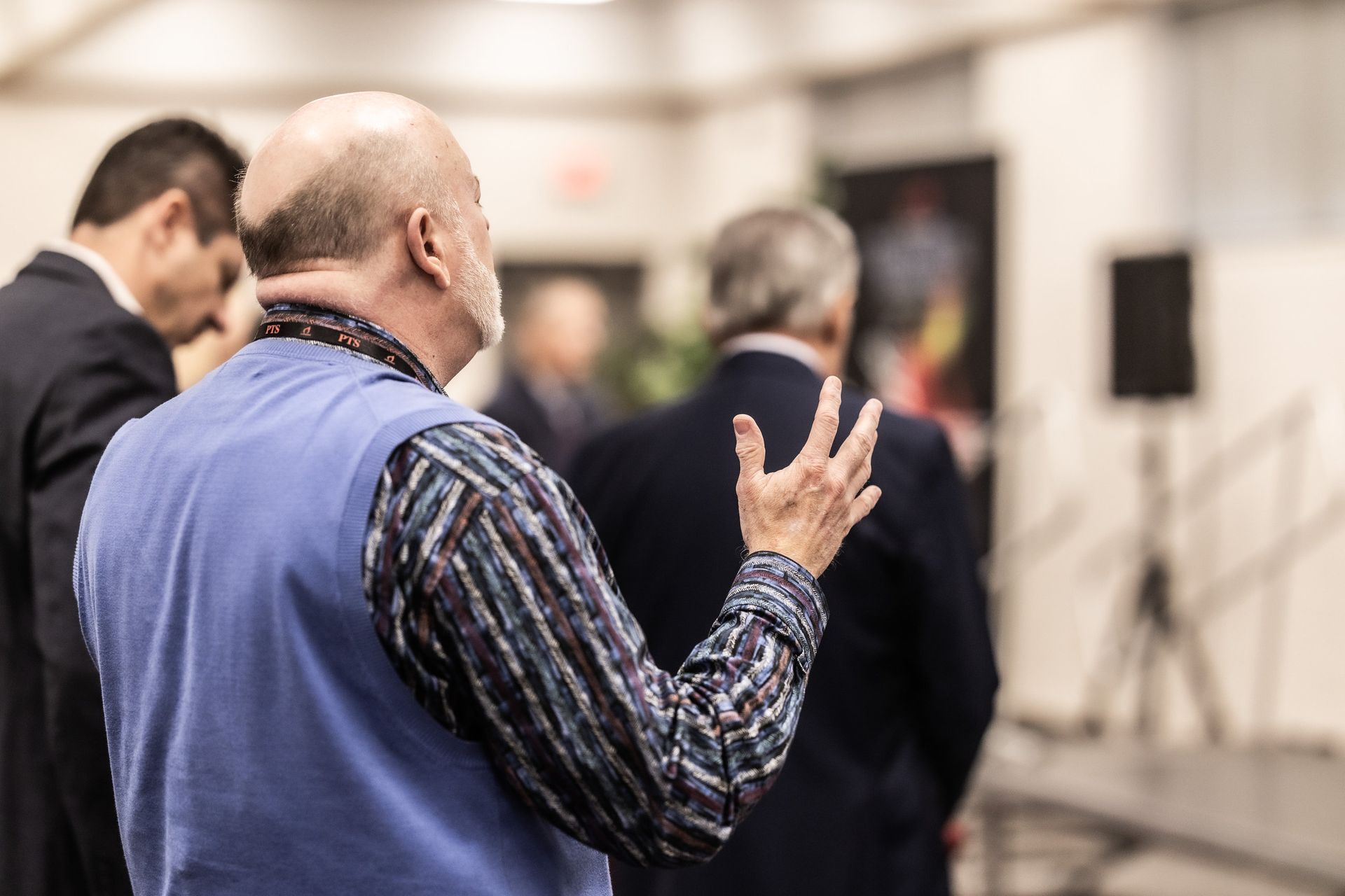 A man with a beard is standing in a room with other men.