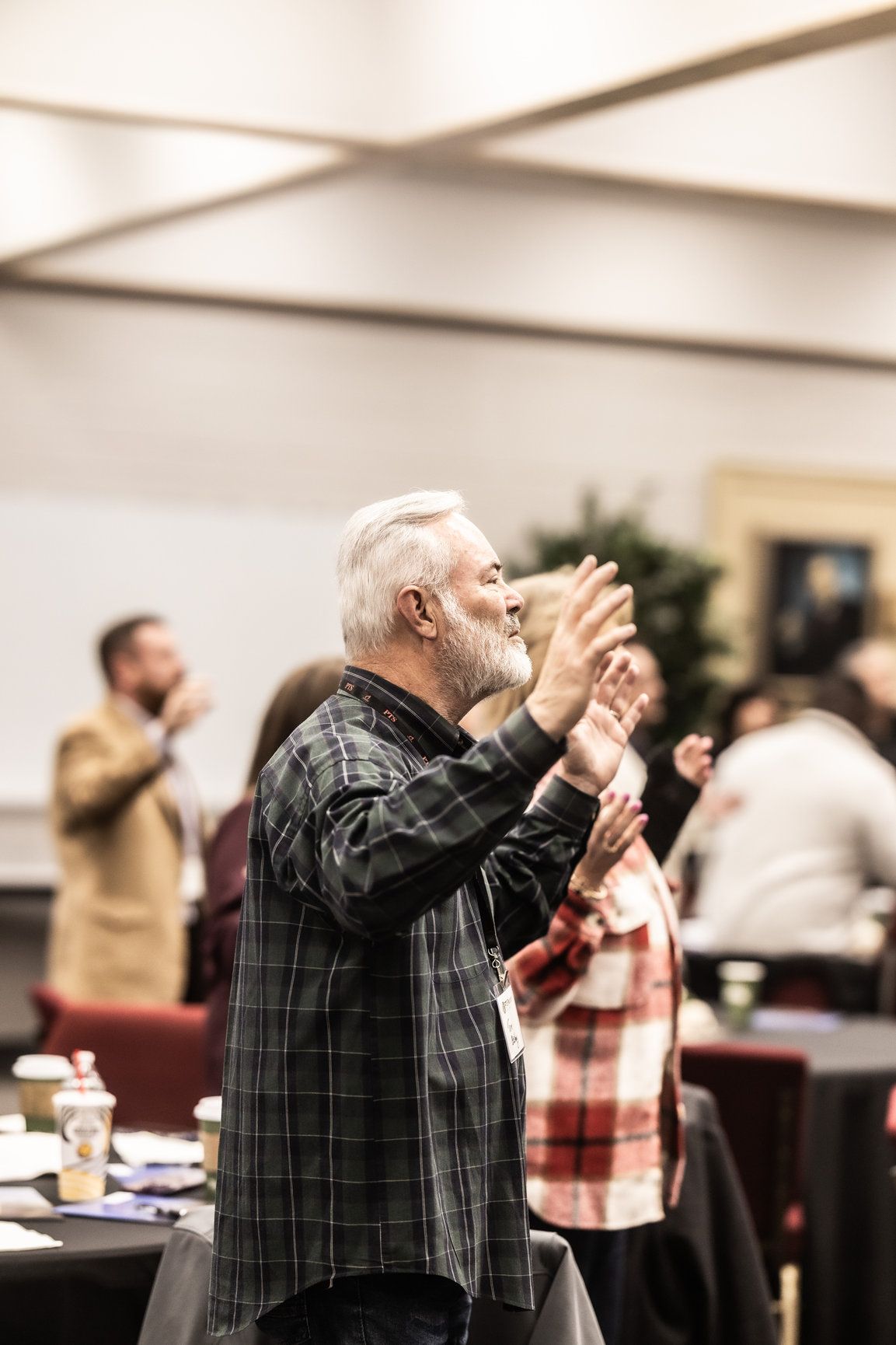 A man with a beard is standing in a room with his hands in the air.