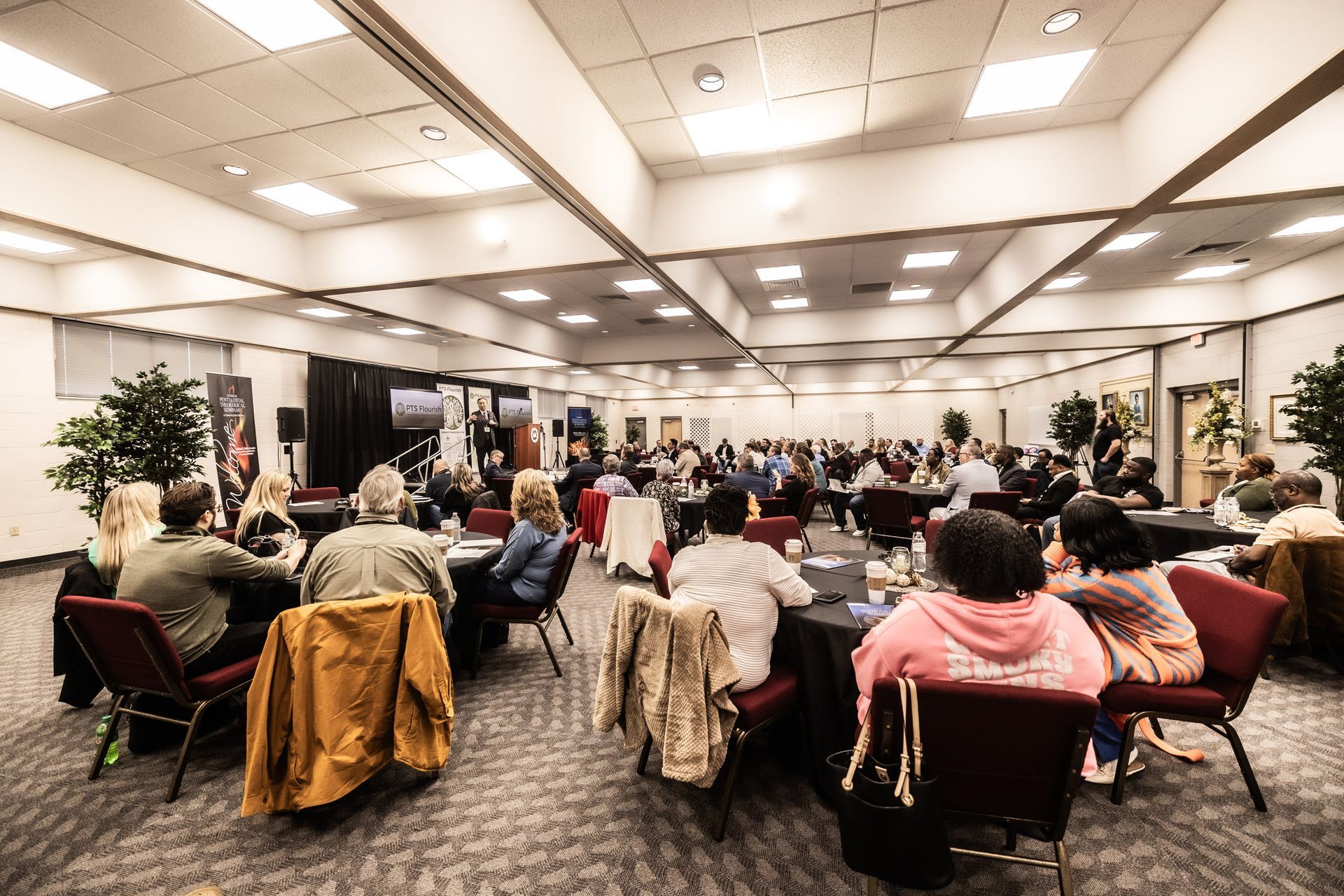 A large room filled with people sitting at tables and chairs.